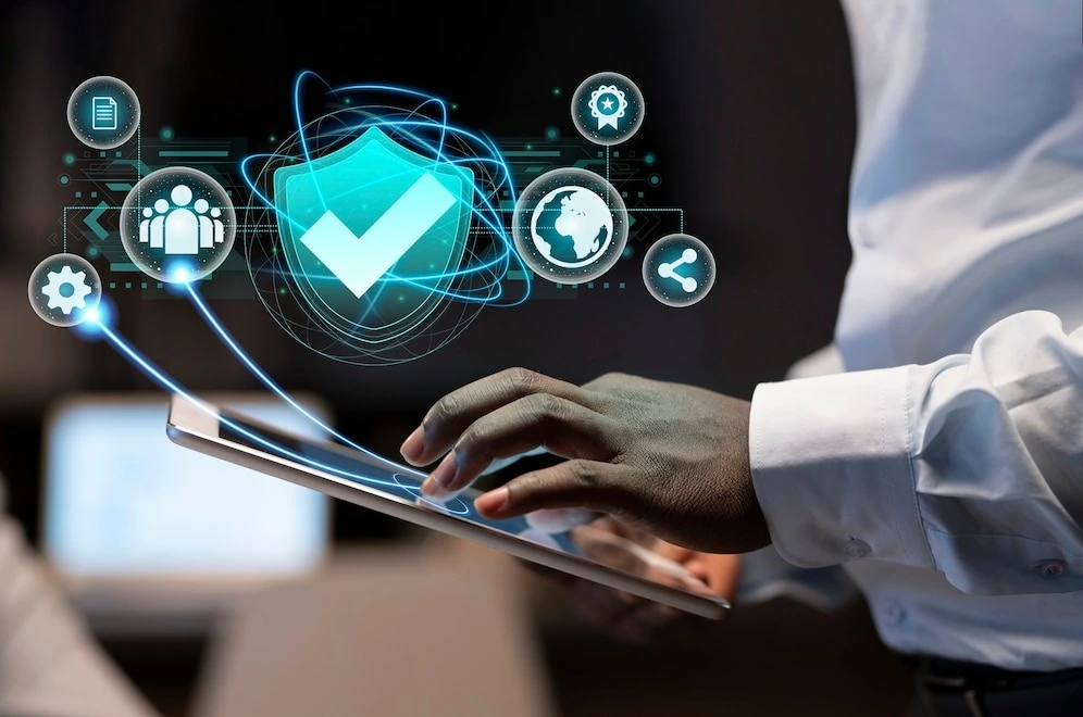 Person using a tablet with graphical overlay of digital icons representing cybersecurity, global connectivity, and technology, including a central security shield, gears, a globe, and a bone-shaped icon