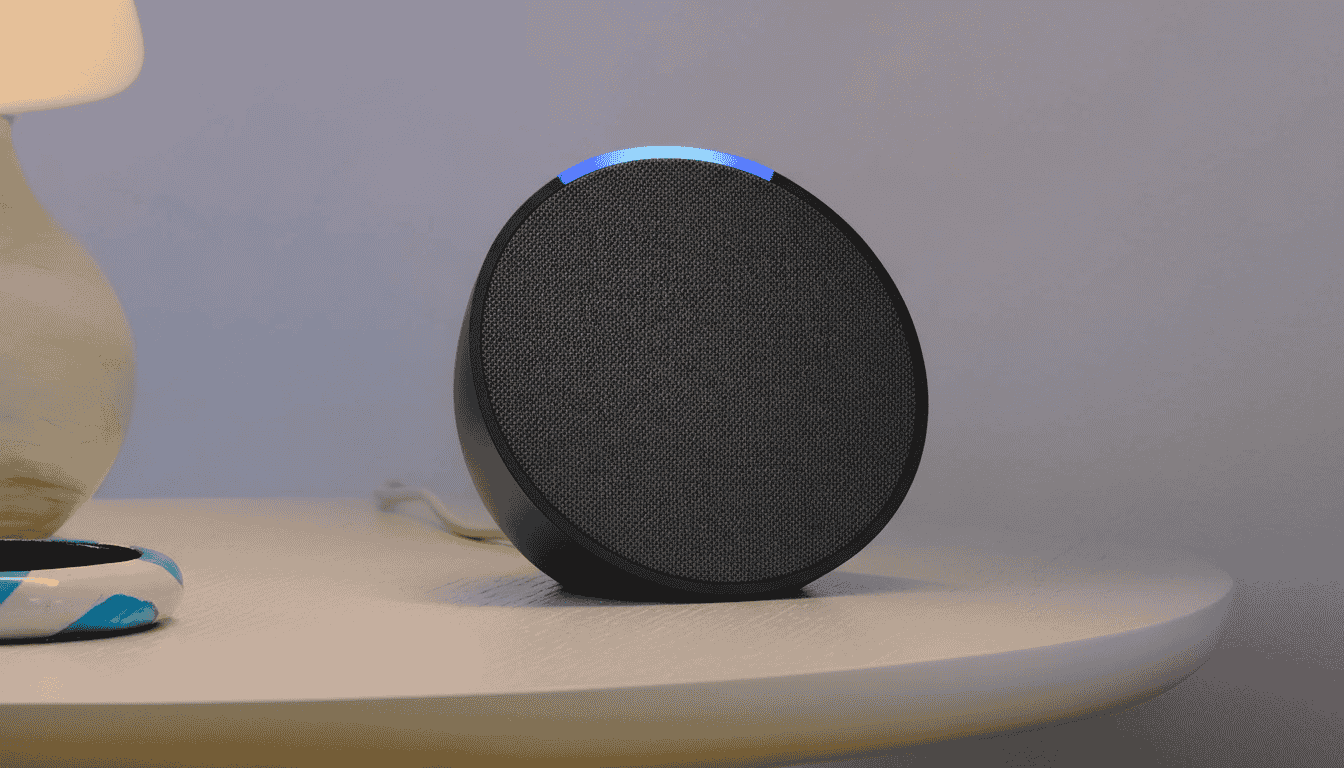 Amazon Echo Pop Amazon Echo Pop speaker with a glowing blue ring sits on a white table. A beige lamp and a colorful coaster are adjacent, creating a minimalist, cozy vibe.