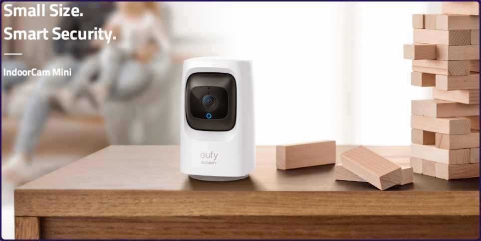 Eufy Security Camera 2K A compact indoor Eufy Security Camera 2K by eufy sits on a wooden table, surrounded by wooden blocks. Text reads "Small Size. Smart Security. IndoorCam Mini."