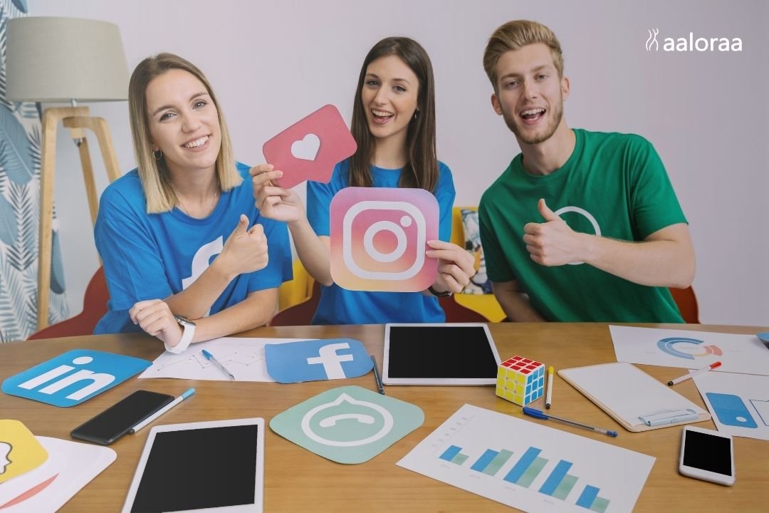 Three smiling young adults sit at a table, holding Instagram and like icons, with social media logos and devices scattered around. The mood is cheerful.